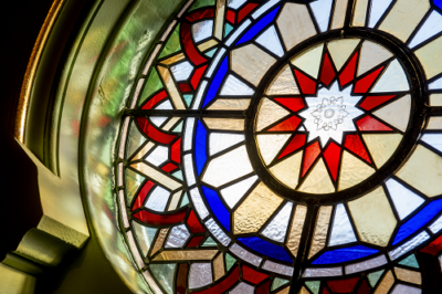 Colourful circular stained glass window with geometrical patterns. Colours that stand out are blue, dark read and light cream.