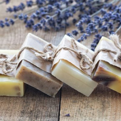 Four bars of handmade soap wrapped in paper and twine, on a wooden surface with lavender sprigs.